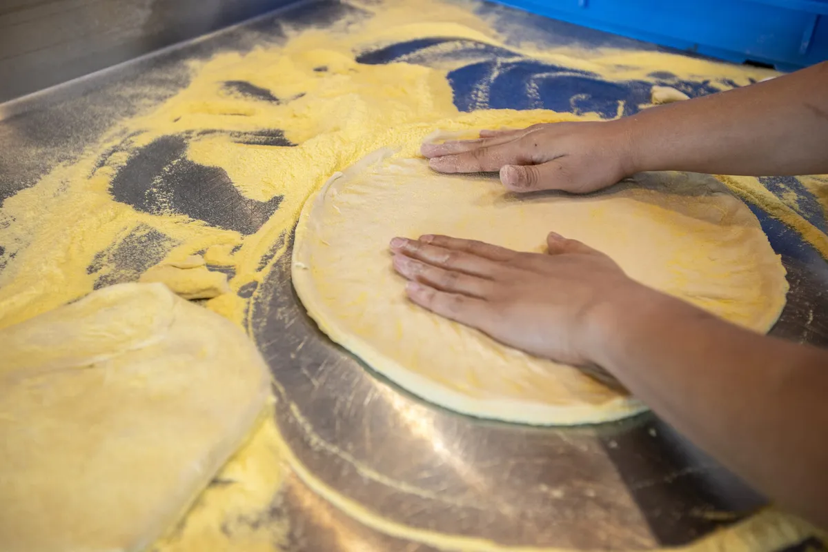 Cook stretching pizza dough on a floured stainless prep table