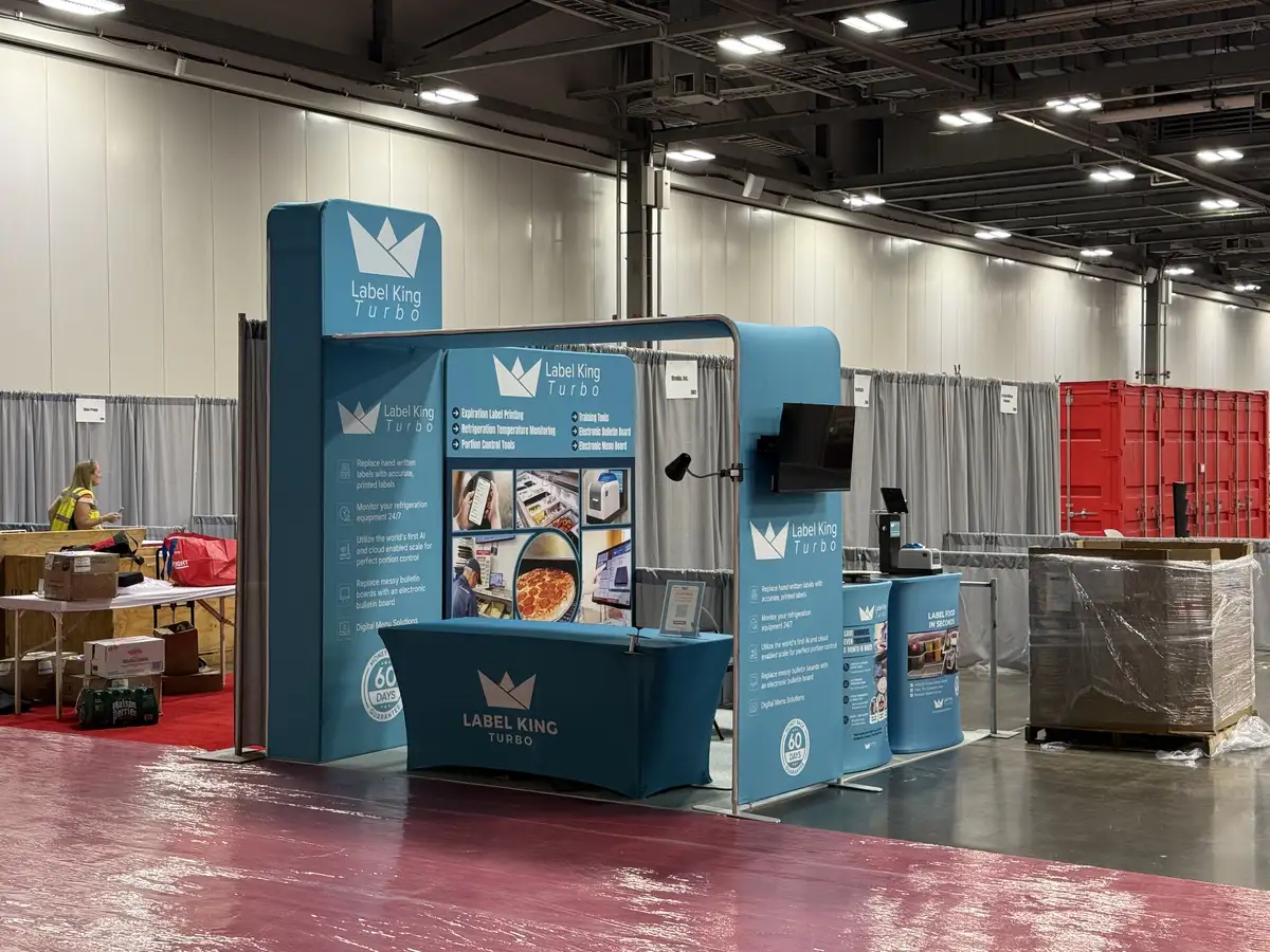 Wide view of the teal Label King Turbo booth at Pizza Expo, with branded towers, demo counters, and a mounted display