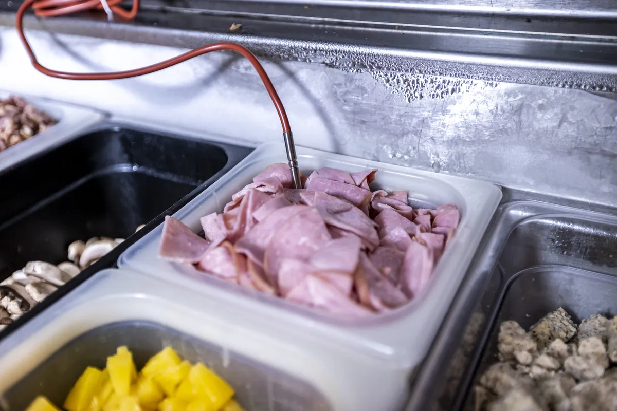 Temperature probe checking a pan of sliced ham in a refrigerated prep station